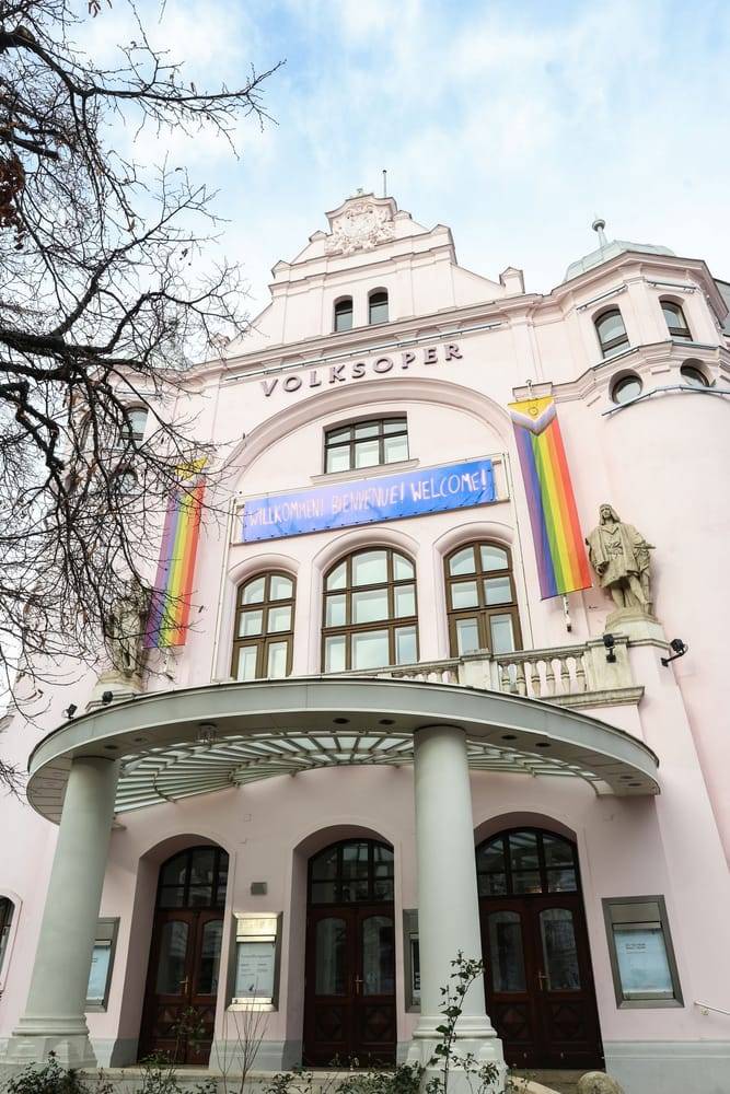 Volksoper from outside with banner with the text "Willkommen, Bienvenue, Welcome" and two rainbow flags to the left and right of the banner