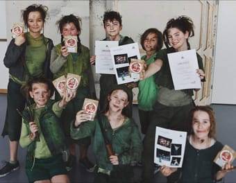 Kinder aus dem Kinderchor der Volksoper in grünen "Peter Pan" Kostümen posiert drinnen für ein Foto und halten die Urkunden für das Schulprojekt und kleine Tüten mit Keksen der Wiener Städtischen in die Kamera.