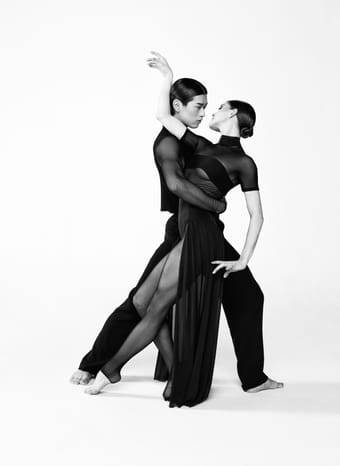 Schwarz-Weiß-Foto eines tanzenden Paars in enger Pose; elegante, ausdrucksstarke Bewegung vor hellem Hintergrund.