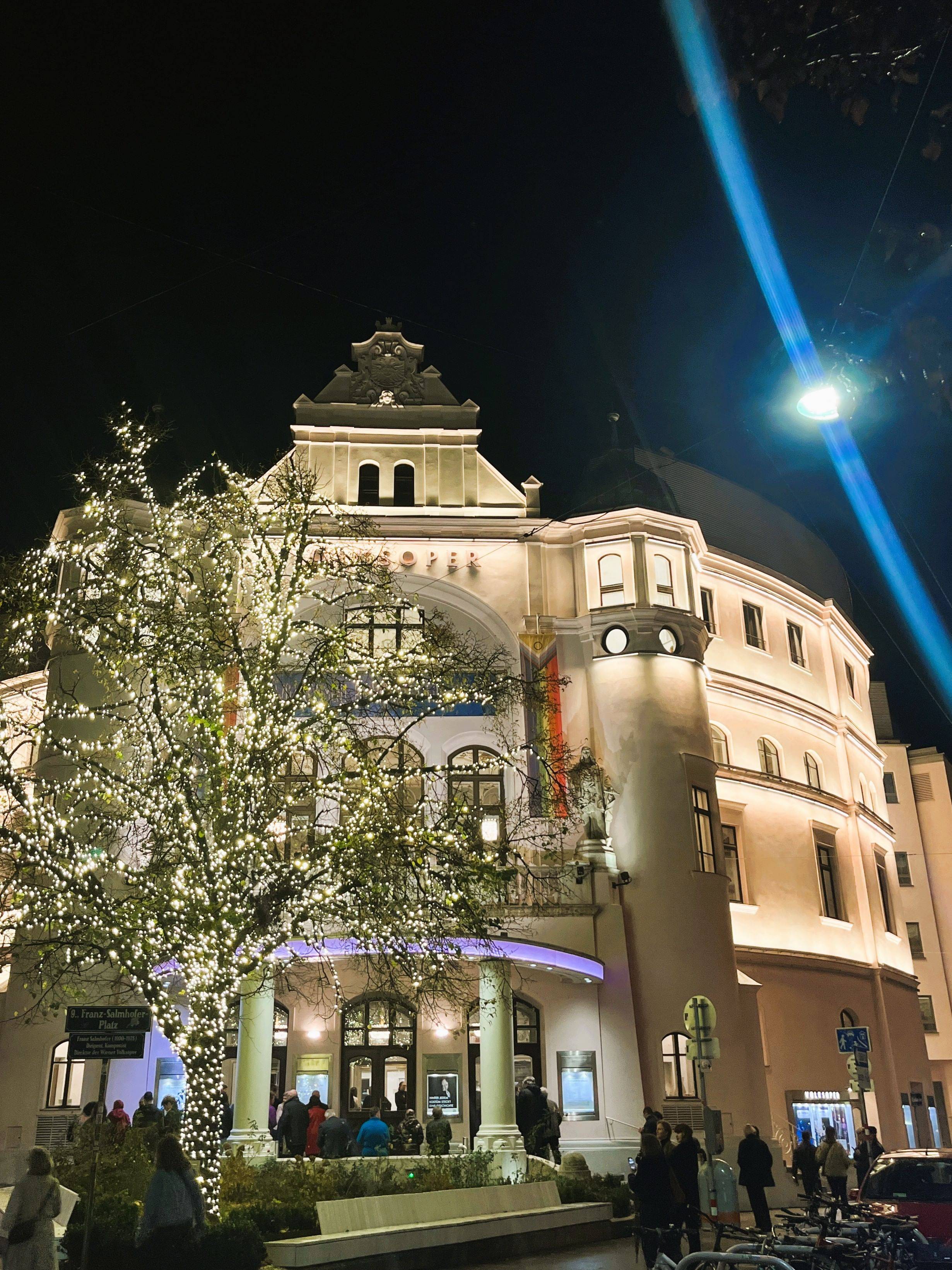 Außenanssicht der Volksoper bei Nacht. Haus und davorstehender Baum sind erleuchtet.