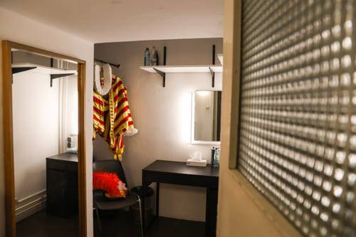 Kleines Zimmer (für Schnellumzüge) mit Spiegel, Tisch und auffälligem rot-gelbem Kostüm.